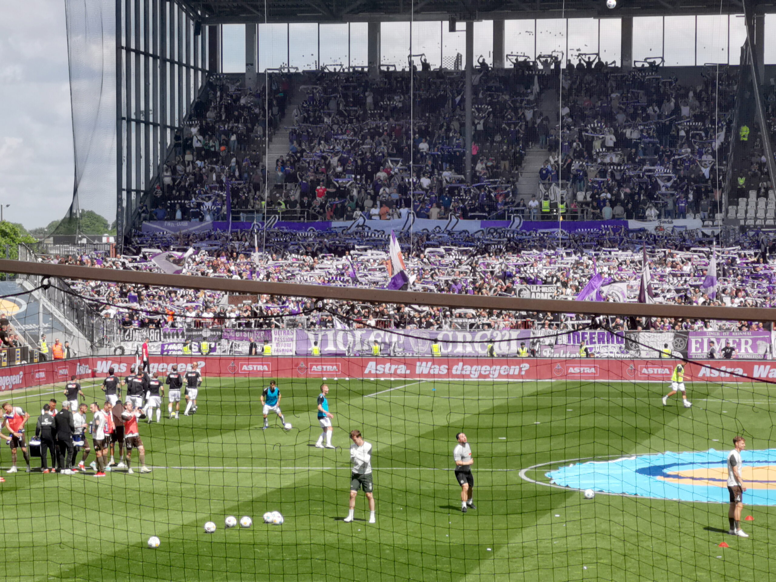 Zu sehen ist der Gästeblock im Millerntor-Stadion mit den Osnabrück-Fans. Im Vordergrund machen sich die Spieler auf dem Rasen warm